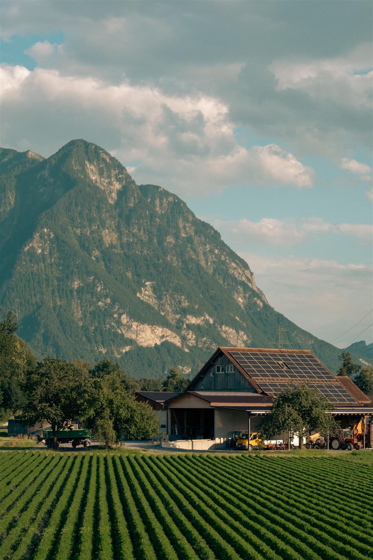 Farm building with rooftop solar beside cultivated fields and mountains